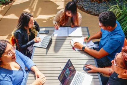 A group of students collaborate at a picnic table outdoors.