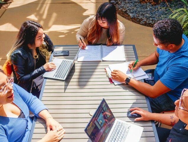 A group of students collaborate at a picnic table outdoors.