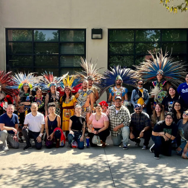 large group of people smiling with some dressed in feathered head dresses