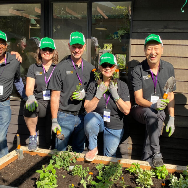 group of people smiling wearing green hats by a raised flower bed