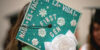 A college graduate's mortar board is decorated with green glitter and white flowers.
