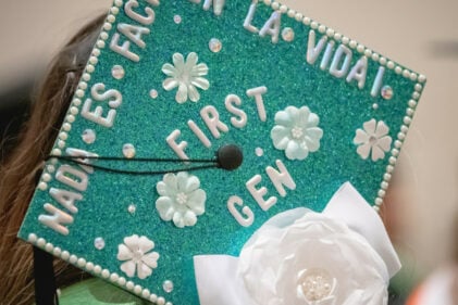 A college graduate's mortar board is decorated with green glitter and white flowers.