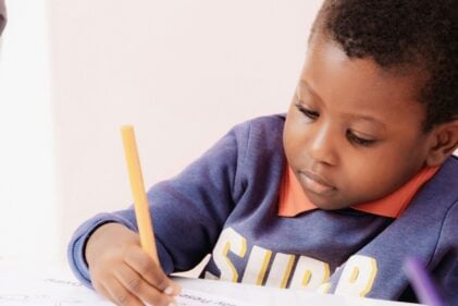 Small child writing in a notebook with a pencil.